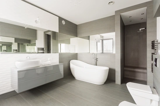 Salle de bain moderne haut de gamme avec baignoire îlot blanche ovale, meuble vasque suspendu gris laqué, double vasque à poser, grande douche à l'italienne carrelée