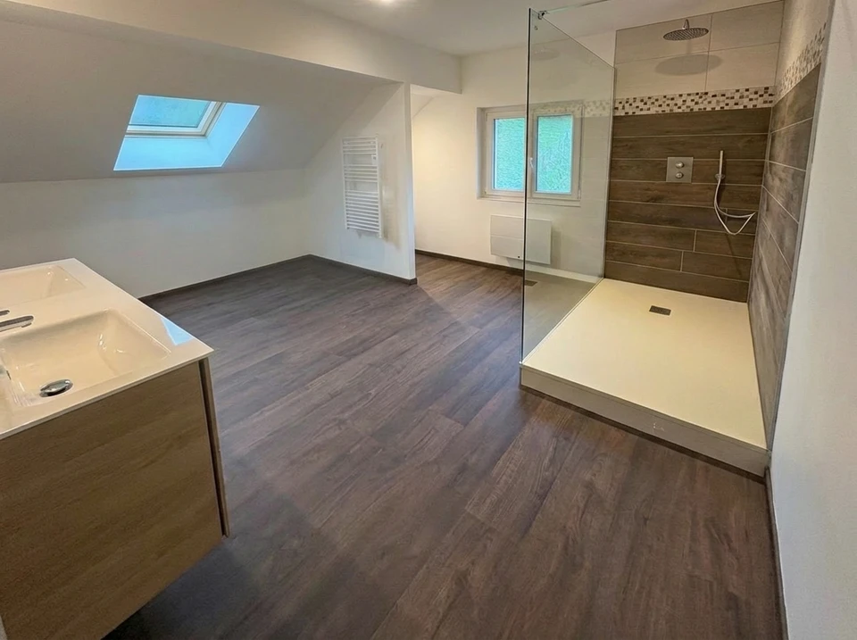 Photographie professionnelle montrant trois artisans en vêtements de travail dans un chantier résidentiel : un plombier avec des outils de plomberie près d'une tuyauterie, un chauffagiste inspectant une chaudière murale, et un couvreur avec équipement de sécurité visible sur le toit ou à proximité de matériaux de toiture. Les trois professionnels sont clairement identifiables et visibles dans le même cadre, travaillant de manière coordonnée sur le même lieu. Cette composition doit transmettre l'idée de polyvalence, de coordination et d'un seul point de contact pour les trois corps de métier.