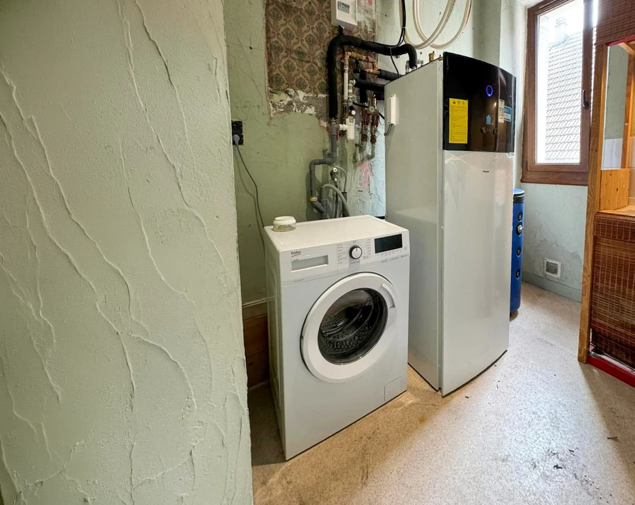 Un plombier en uniforme bleu travaille sur une toilette blanche, tenant une clé à molette jaune et noire d'une main tout en manipulant le mécanisme de chasse d'eau de l'autre