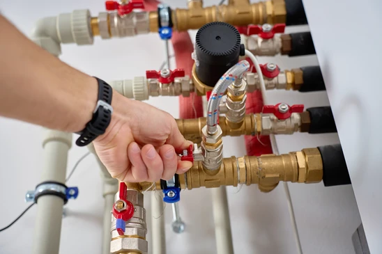 Technicien en combinaison rouge effectuant la maintenance d'une chaudière domestique dans un local technique